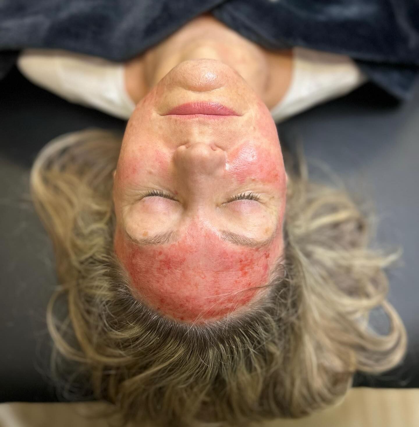 A woman is laying on her back with her head upside down and her eyes closed.