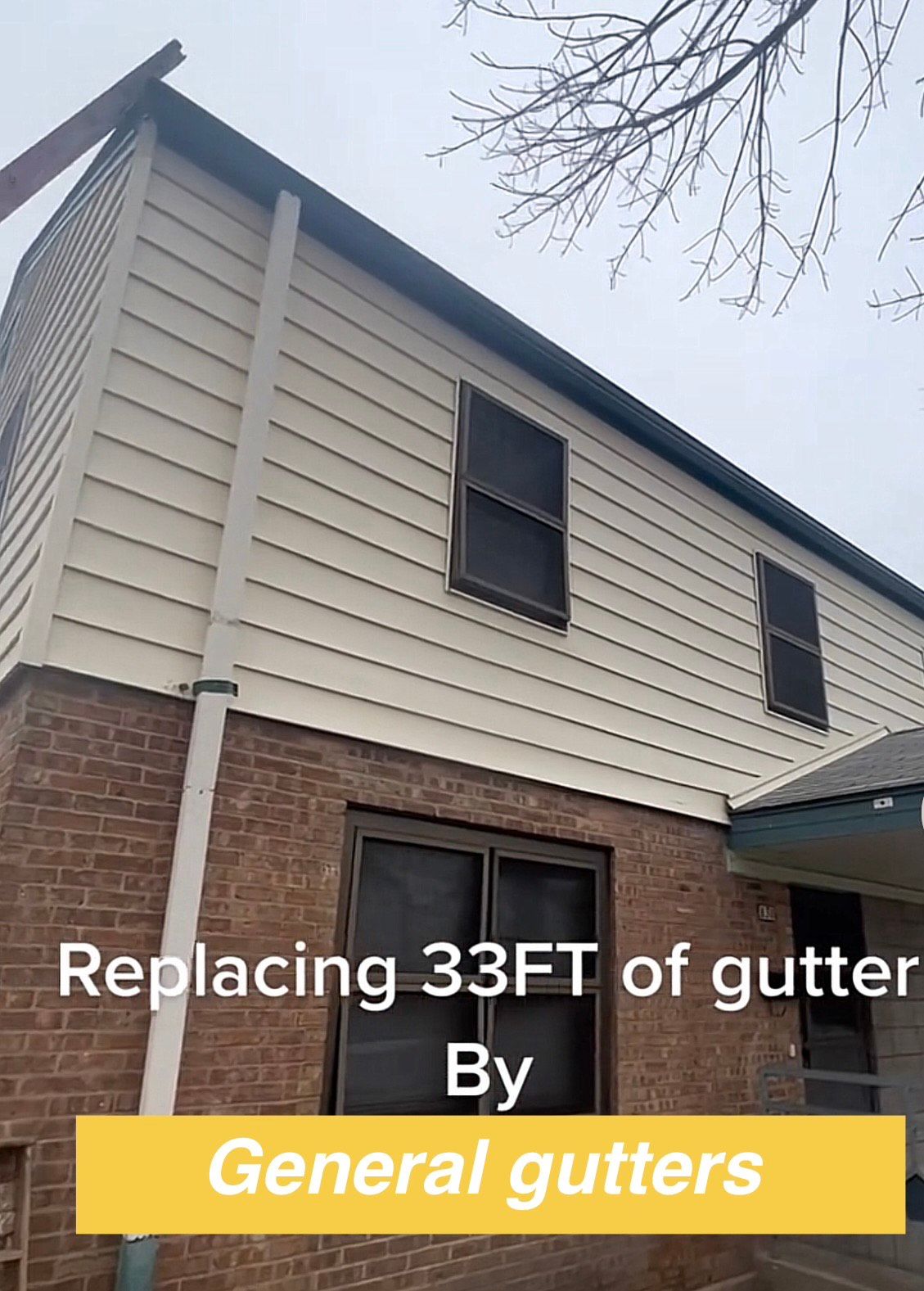 Two-story building with tan siding and brick base. Text says 