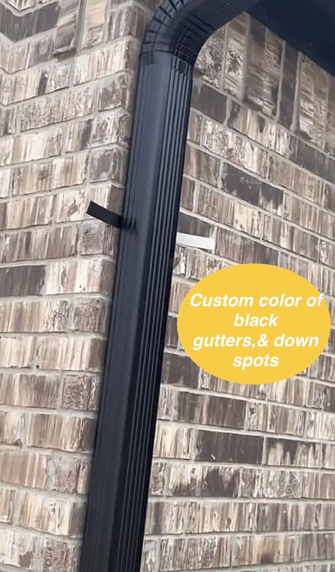 Black gutters and downspout on a brick building with text bubble: 