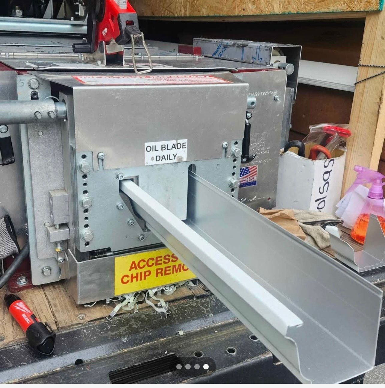 Gutter cutting machine with white gutter, metal body, and warning labels.