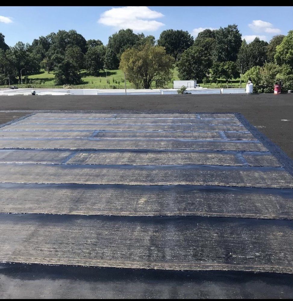 Black flat roof with newly applied sealant in a grid pattern; trees and sky in the background.