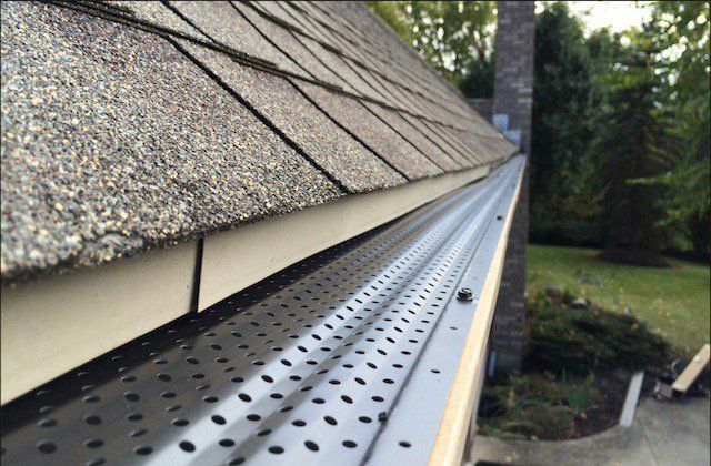 Gutter with metal mesh, installed under asphalt shingle roof.