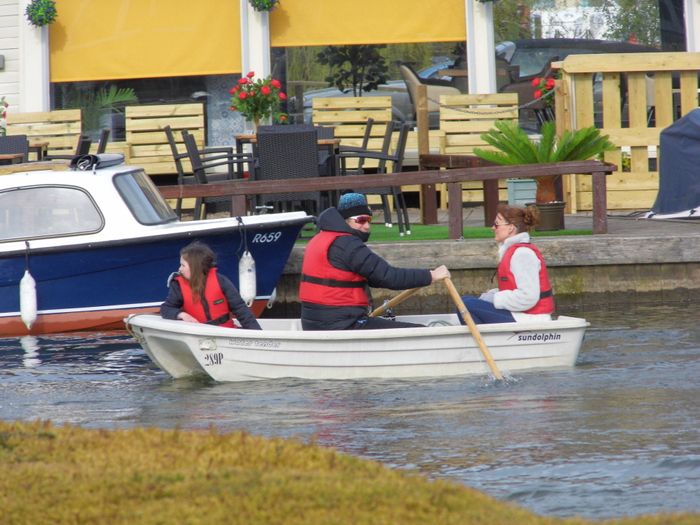 Three people in rowing boat on calm water on River Bure, Norfolk Broads.