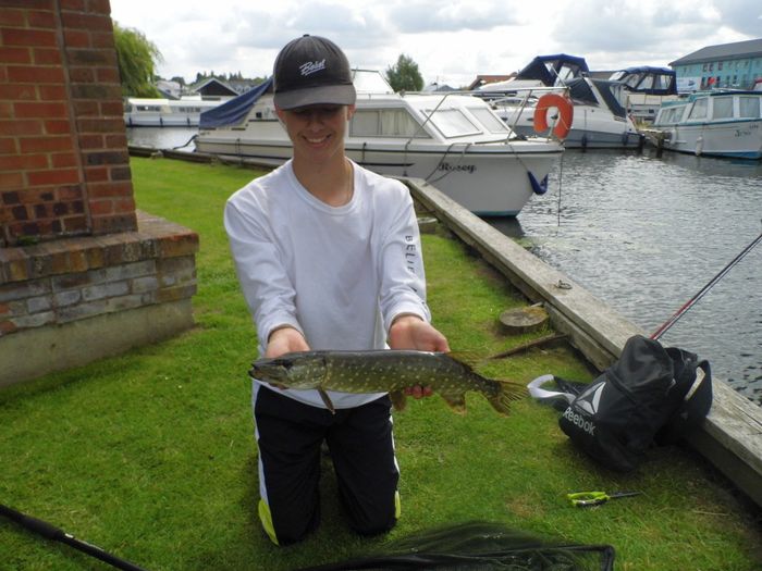 Teenage boy showing of small pike he has just caught.