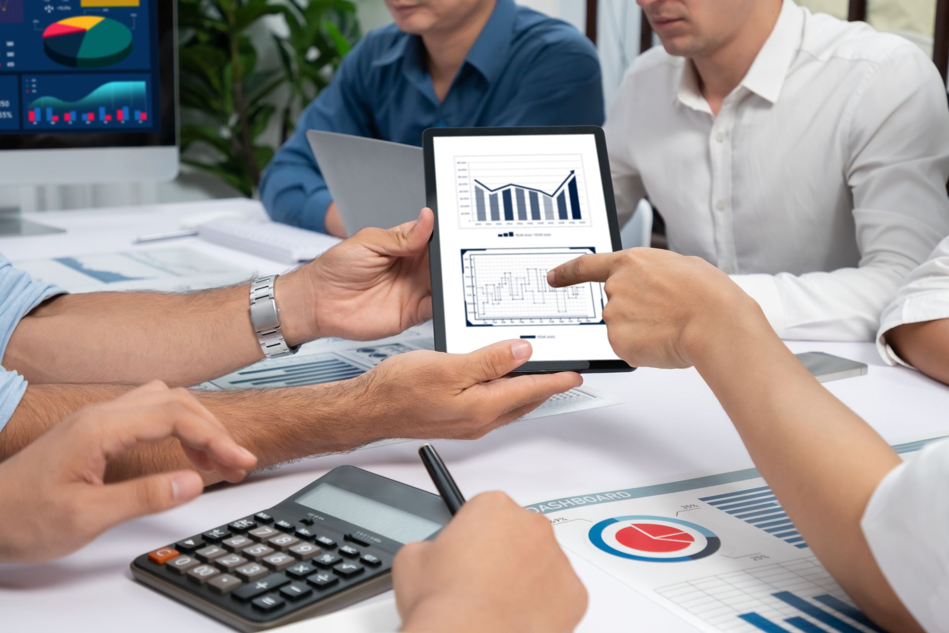 A group of people are sitting around a table looking at a tablet.