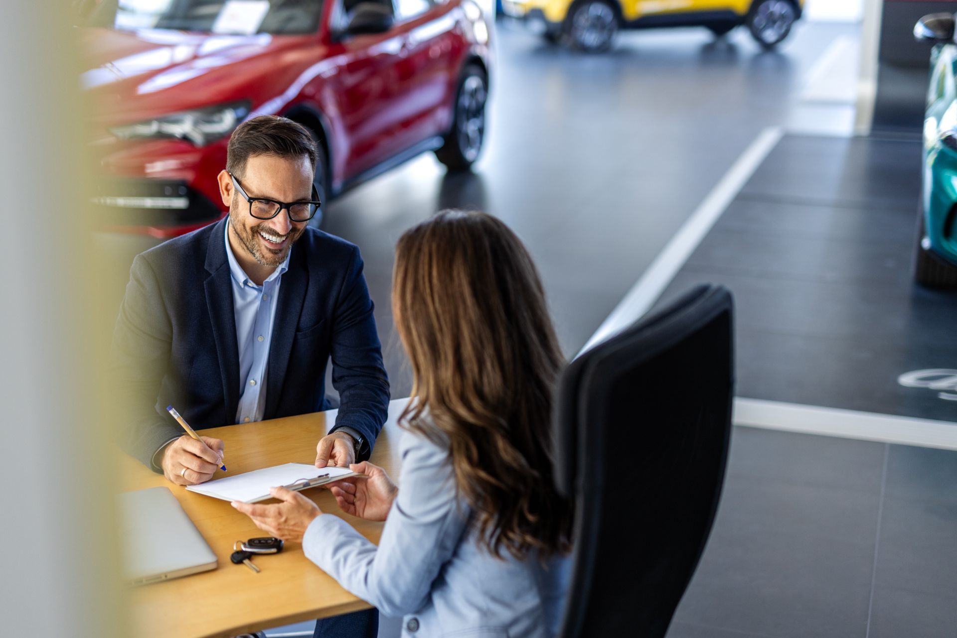 A man and a woman are sitting at a table in a car showroom.