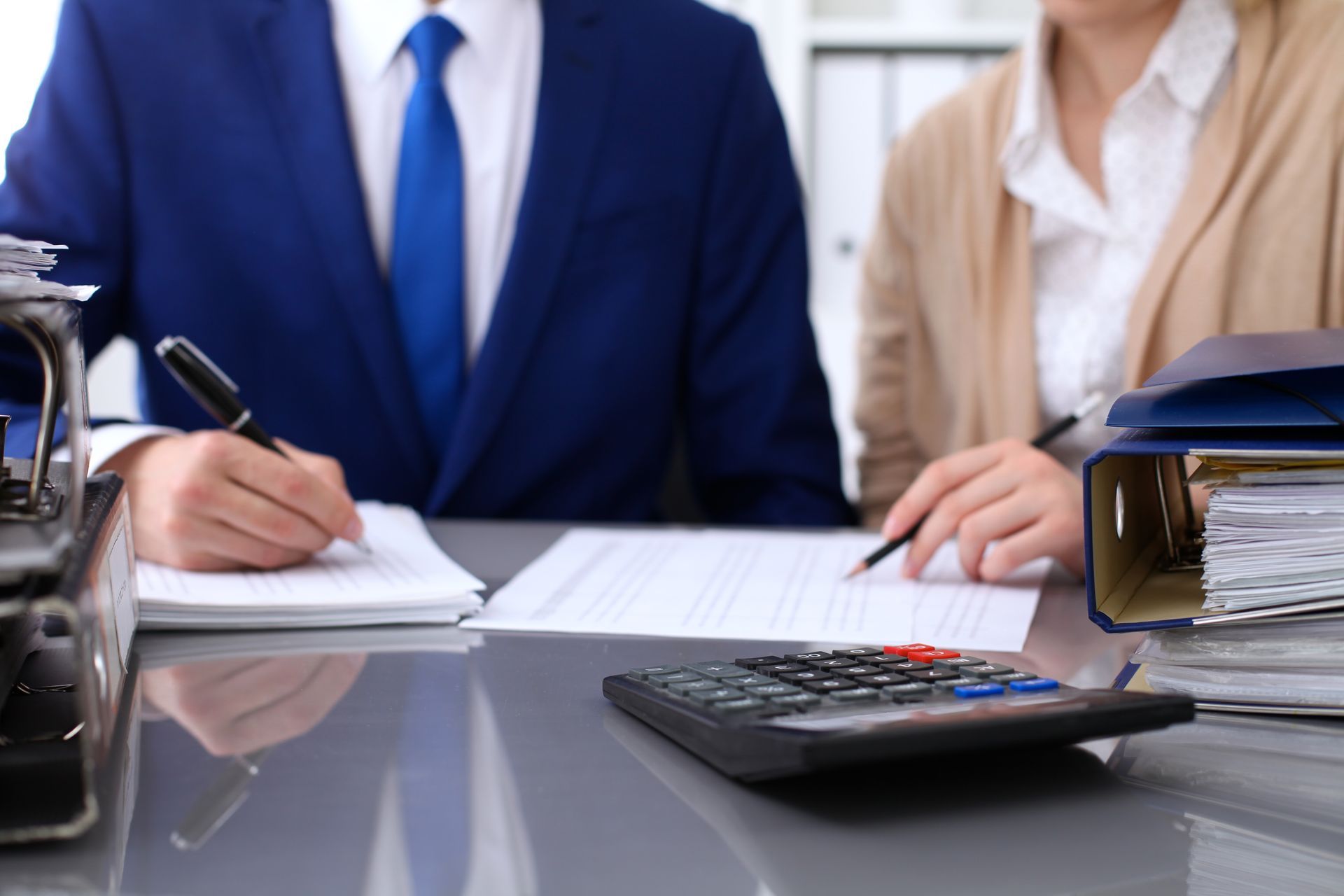 A man and a woman are sitting at a desk with a calculator.