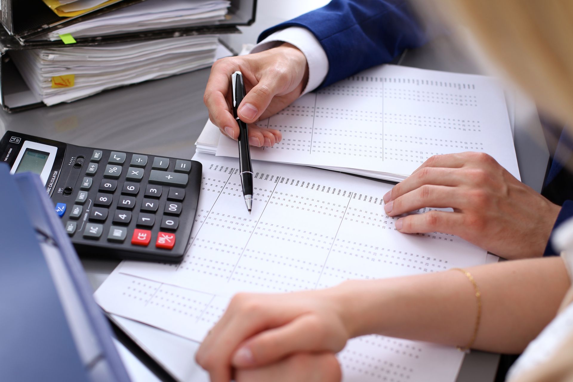 A man and a woman are sitting at a desk using a calculator and a pen.