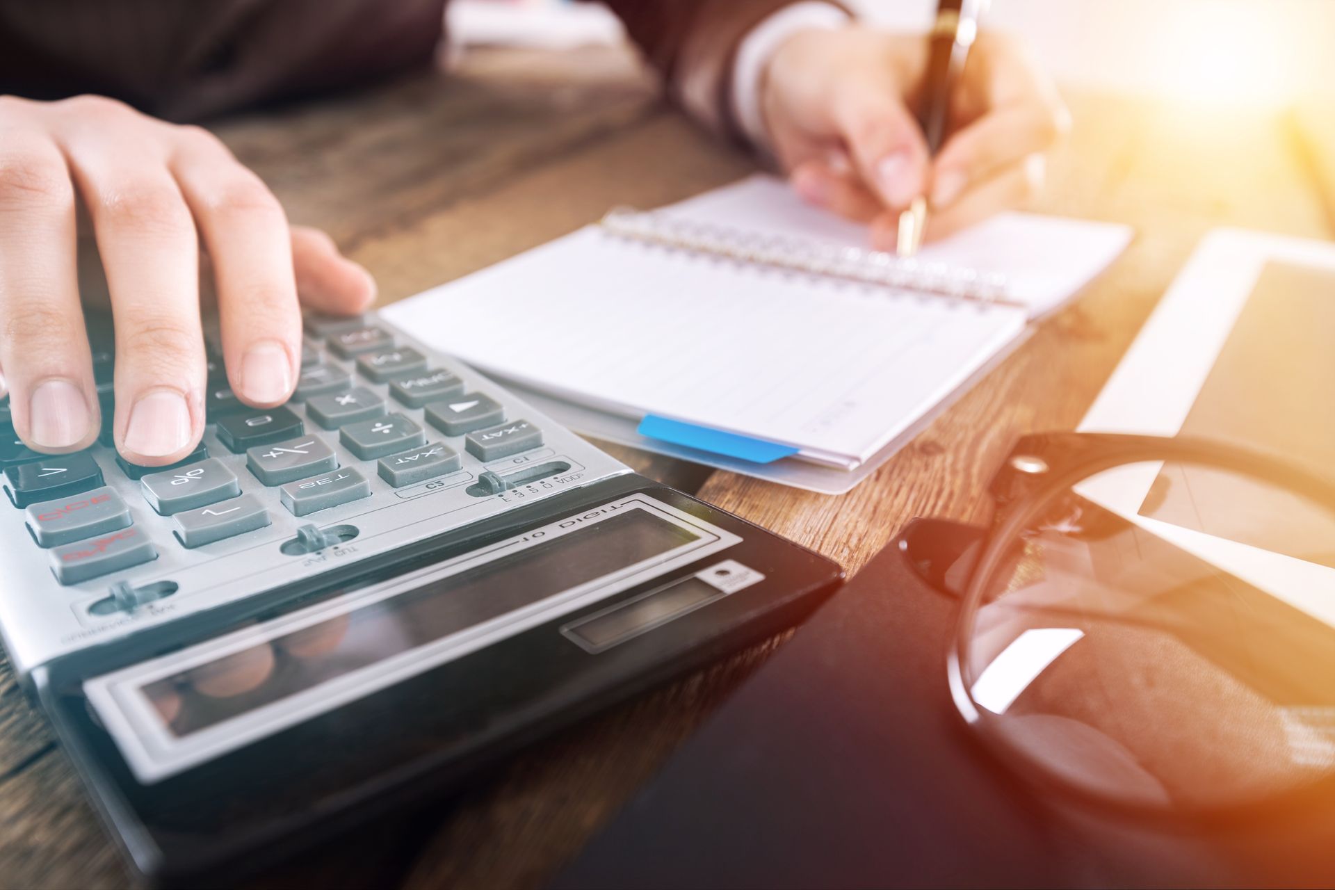 A person is using a calculator and writing in a notebook.