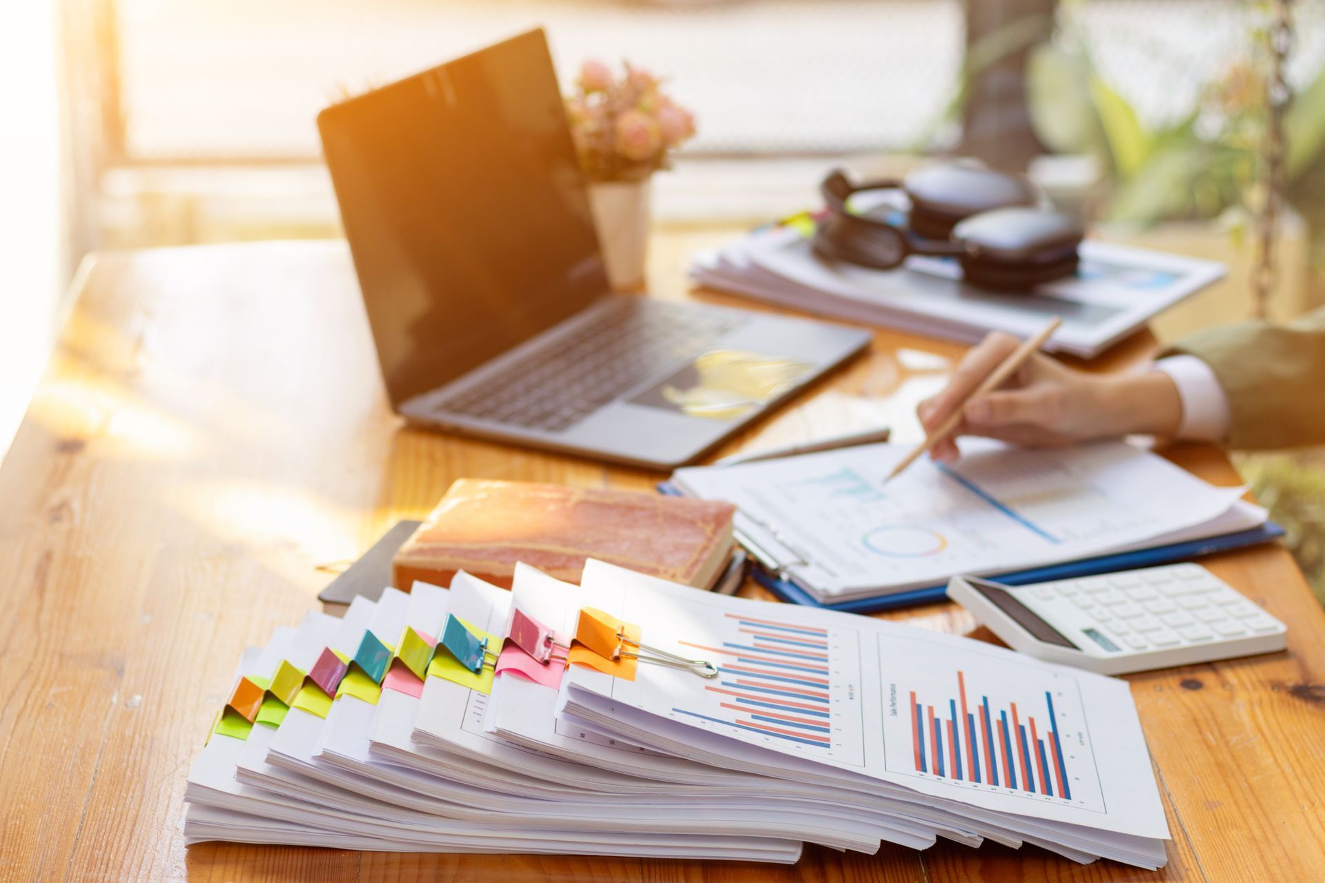 A person is sitting at a desk with a laptop and a stack of papers.