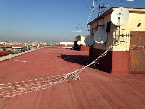 una pavimentazione di un tetto impermeabilizzato di color rosso e delle parabole con cavi a vista