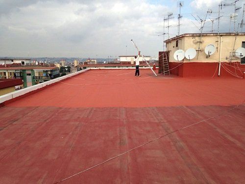 La pavimentazione di un tetto impermeabilizzato di color rosso e un uomo al lavoro