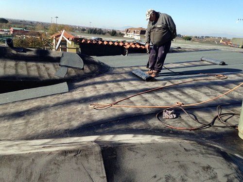 Un uomo in piedi che guarda un rotolo di tessuto impermeabilizzante  posto sulla pavimentazione di un tetto