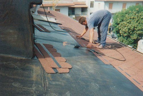 Un uomo chinato in avanti mentre fissa delle tegole di un tetto