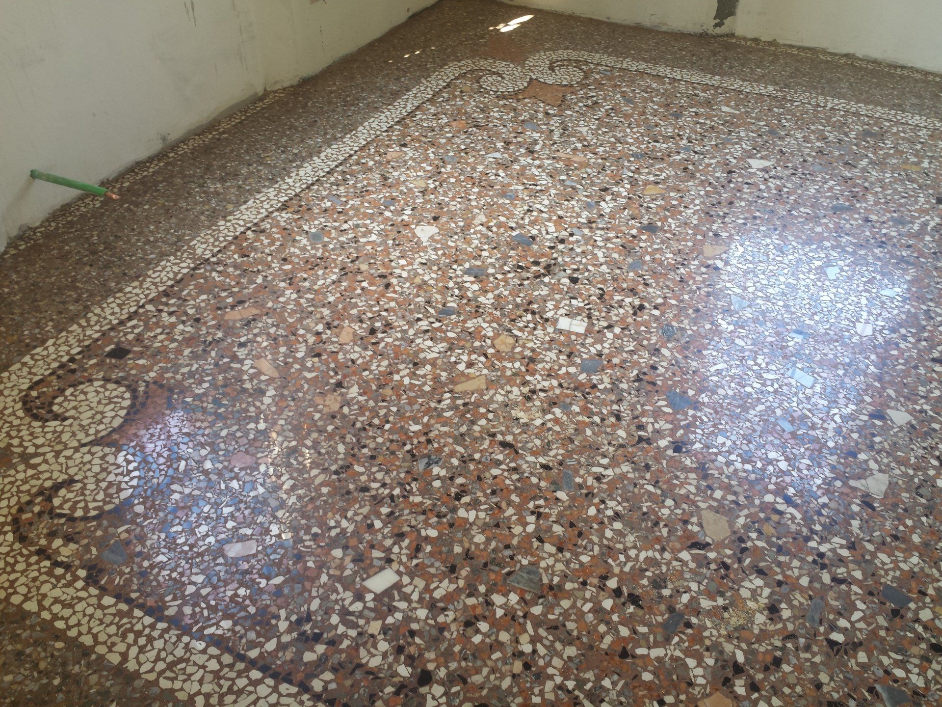 Primo piano di un pavimento in terrazzo lucidato con bordo in mosaico bianco e dettagli decorativi agli angoli.