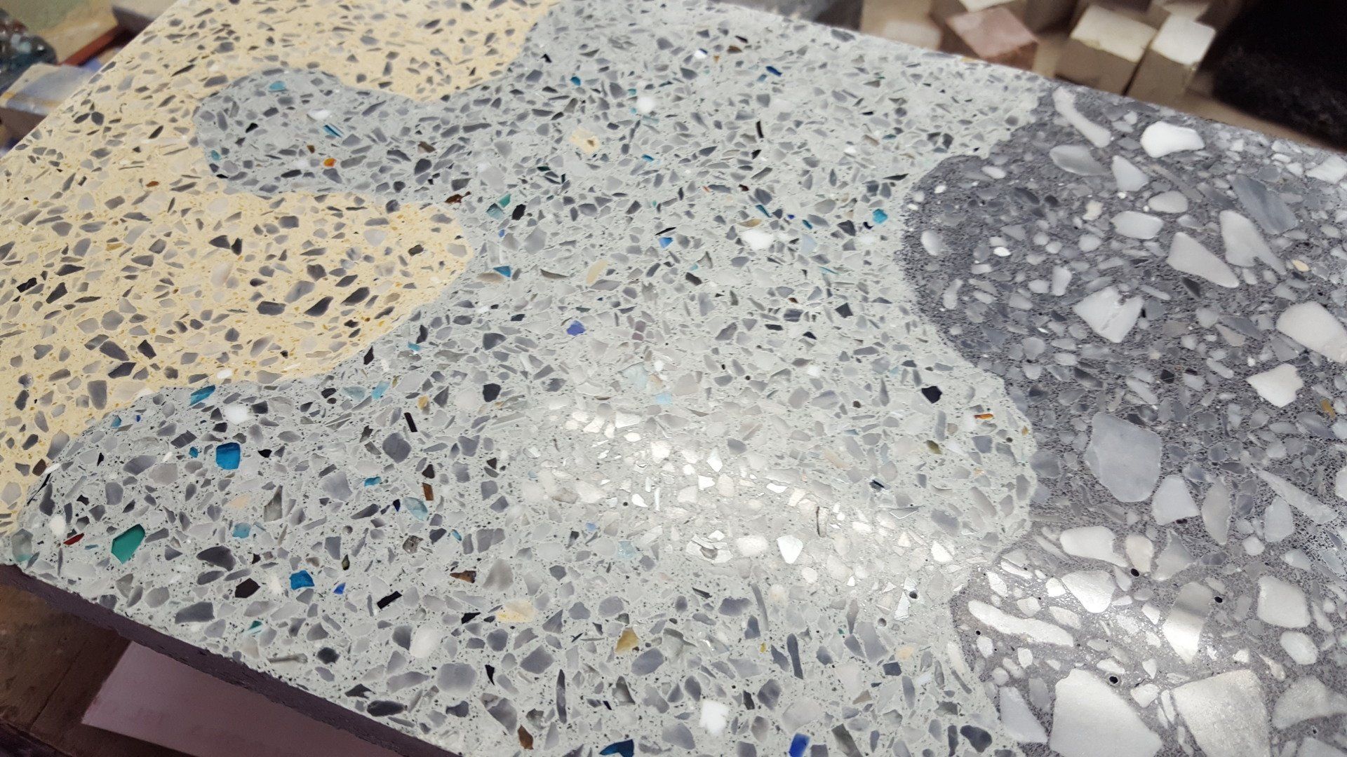 Primo piano di una superficie in terrazzo lucidato con tre forme intrecciate, simili a pezzi di puzzle, nei colori beige, grigio chiaro e antracite.