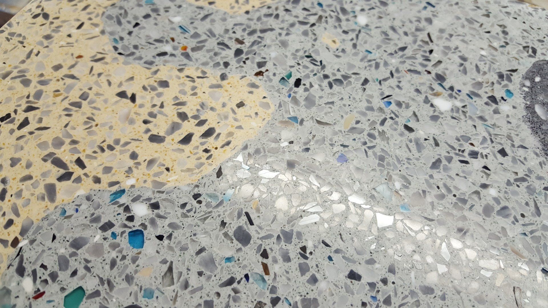 Primo piano di una superficie in terrazzo lucidata con frammenti di pietra e vetro lisci e multicolori su basi grigie e crema.