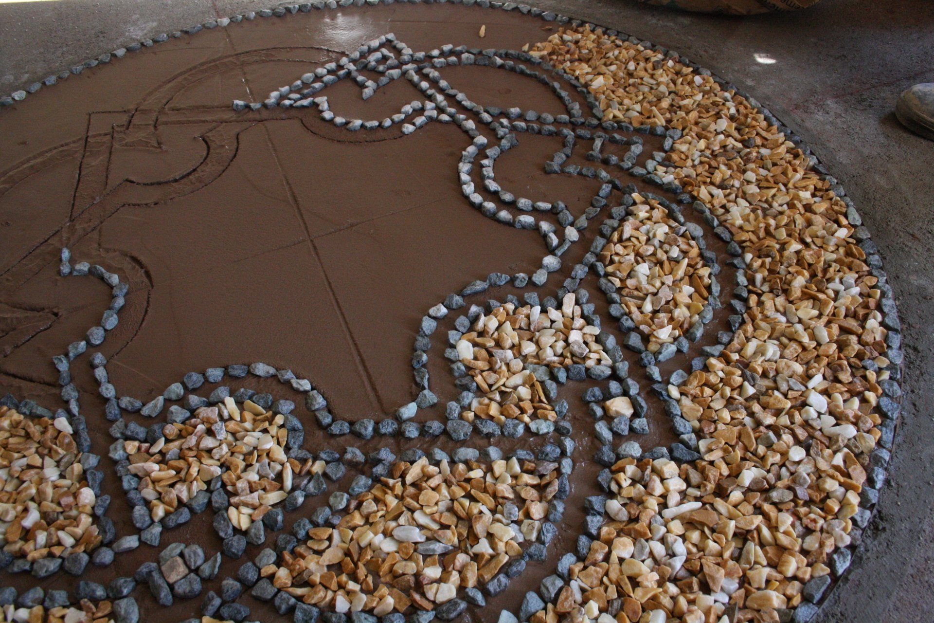Un pavimento a mosaico circolare con ciottoli scuri che formano un intricato motivo a nodi celtici su pietre color marrone chiaro.