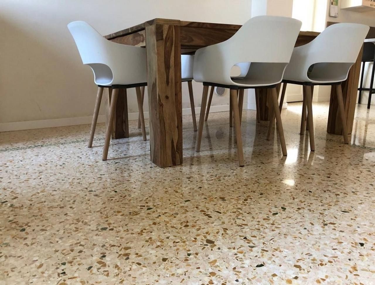 Tre sedie bianche moderne con gambe in legno circondano un tavolo da pranzo in legno su un pavimento in terrazzo lucido e punteggiato.