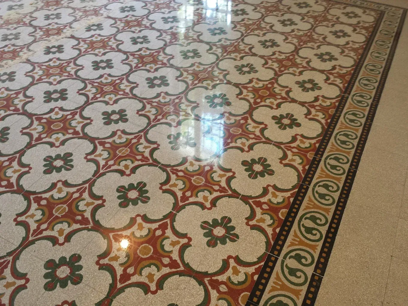 Pavimento lucidato caratterizzato da un motivo ripetuto a quadrifoglio bianco, verde e rosso, bordato da una finitura floreale decorativa.