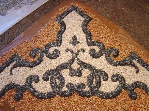 Un motivo decorativo costituito da ghiaia scura inserita in un letto di ciottoli chiari, su uno sfondo di ghiaia marrone.