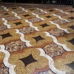 Un motivo di pavimento piastrellato caratterizzato da forme beige a quattro lobi con centri scuri, delineate da bordi bianchi ondulati su uno sfondo screziato.