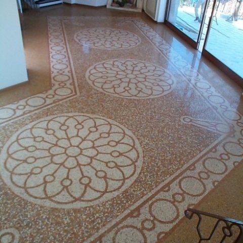 Un pavimento in terracotta lucidato caratterizzato da intricati motivi a rosette circolari dai colori chiari e da bordature decorative.