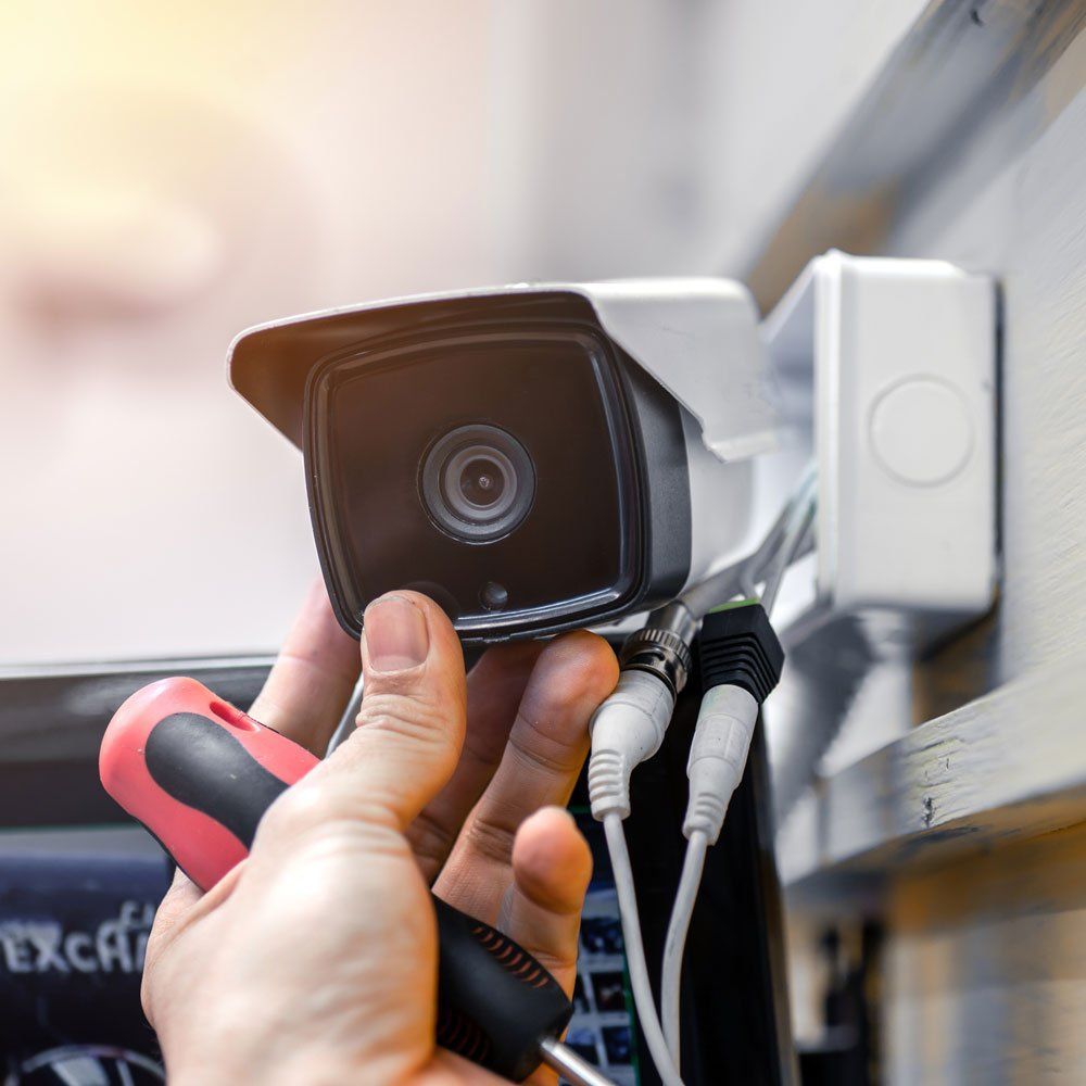 A person is fixing a security camera with a screwdriver.