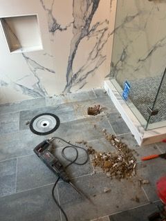 A drill is sitting on the floor of a bathroom next to a shower stall.