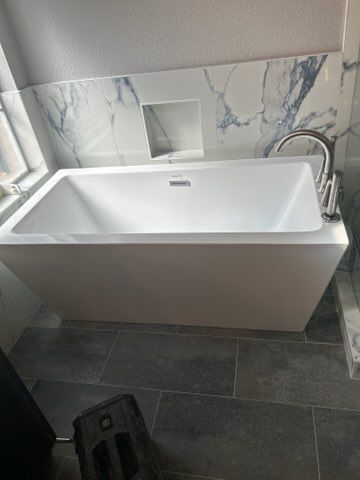 A white bathtub is sitting in a bathroom next to a window.