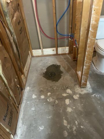 A bathroom with a toilet and a drain on the floor.