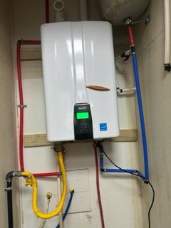 A white water heater is hanging on a wall next to pipes.