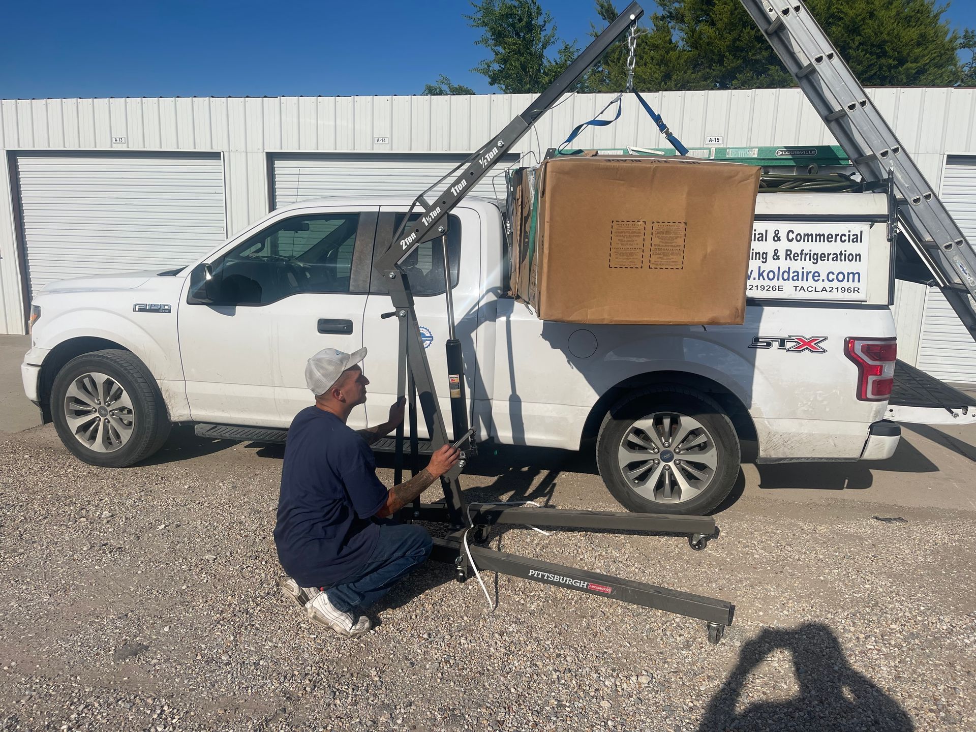 A man is kneeling next to a white truck with a box on top of it.