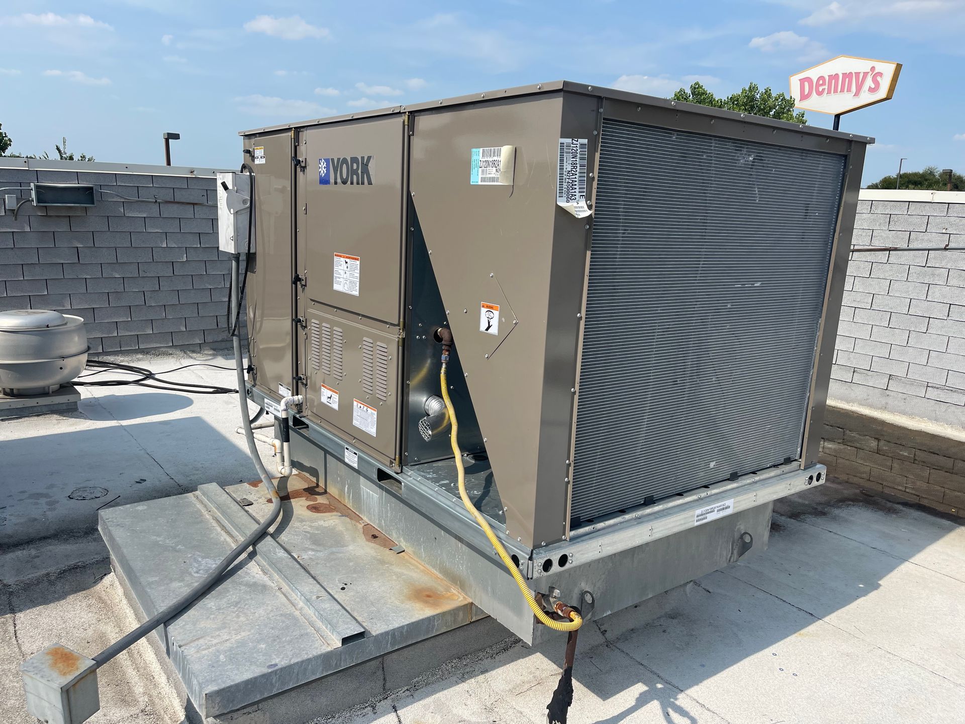 A large air conditioner is sitting on top of a roof next to a danby 's sign.