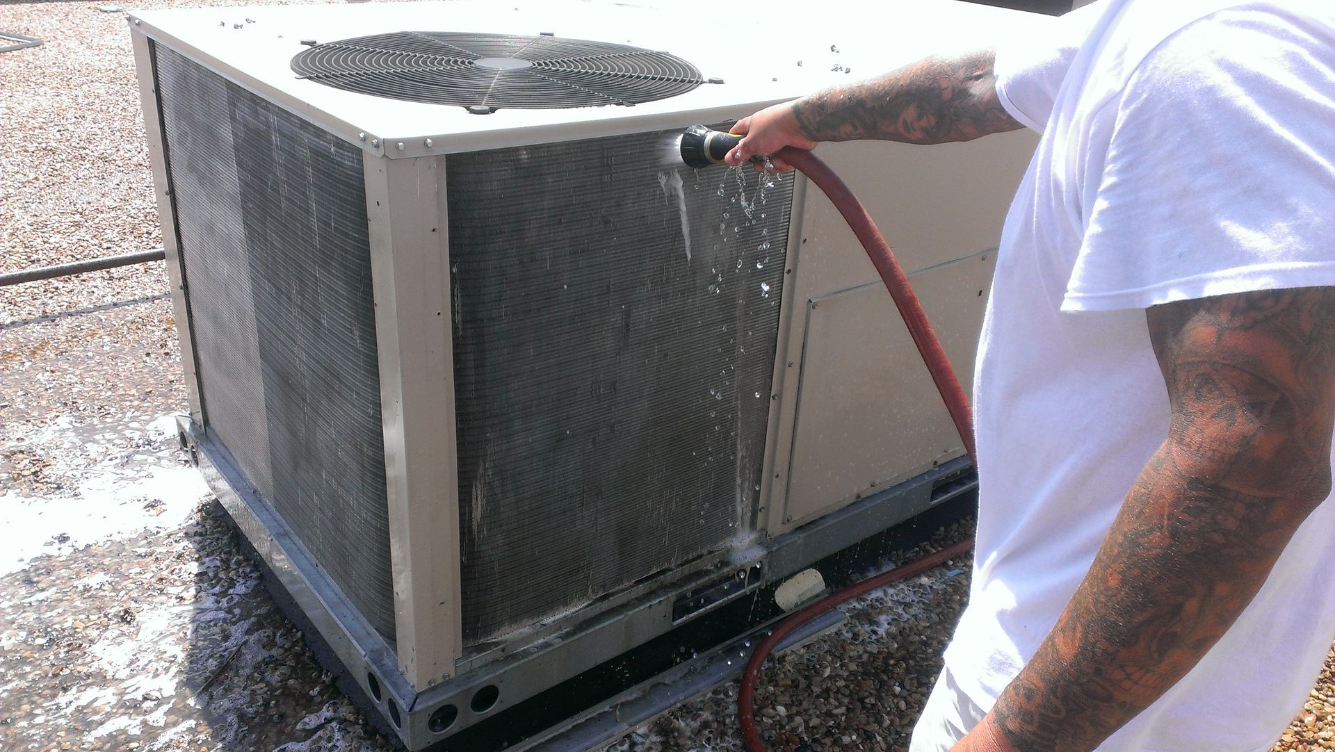 A man is cleaning an air conditioner with a hose