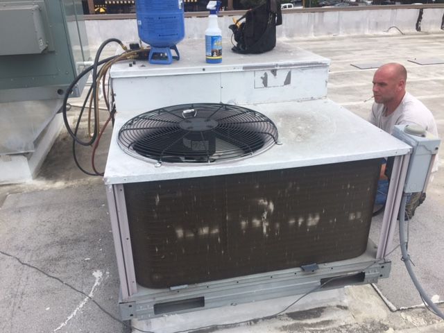A man is working on an air conditioner on the roof of a building.