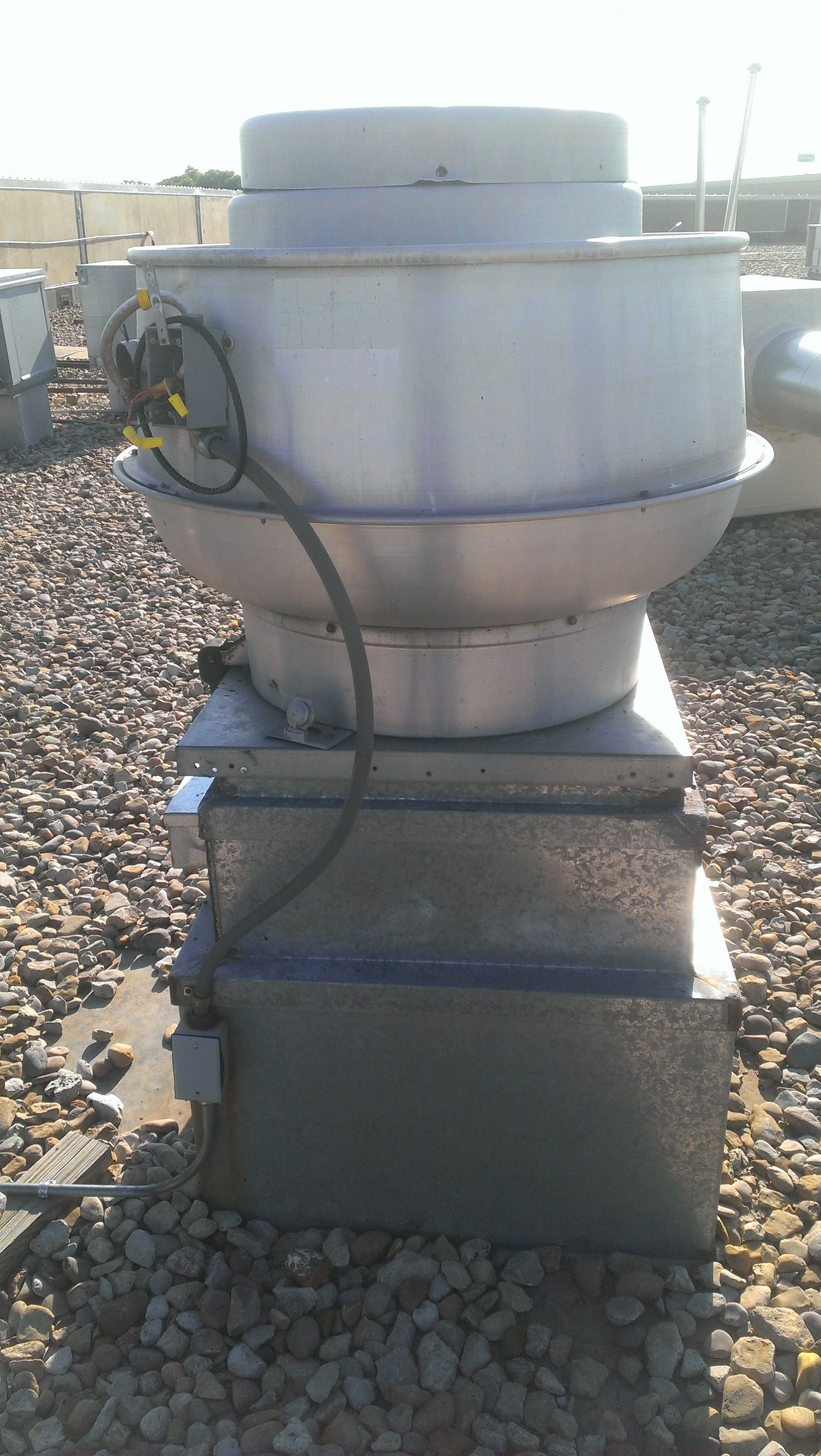 A white exhaust fan is sitting on top of a pile of gravel.