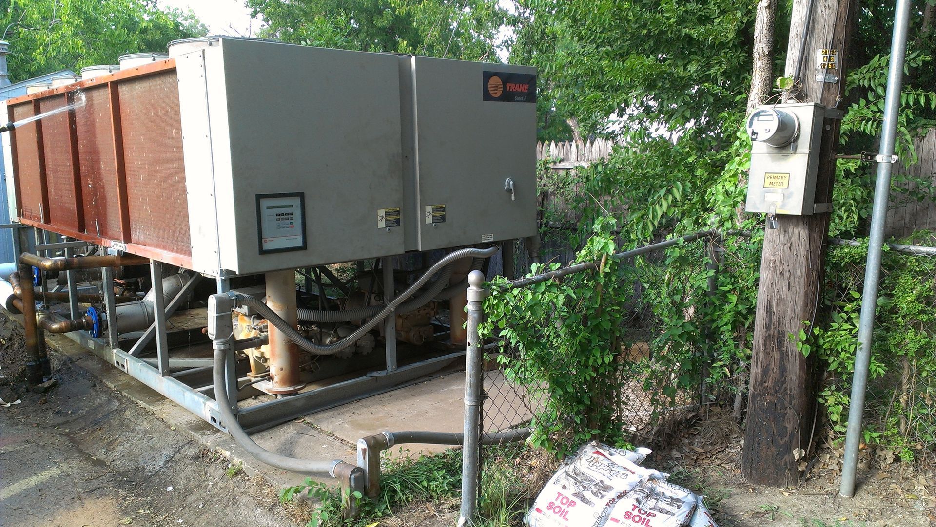 A large gray box is sitting next to a tree.
