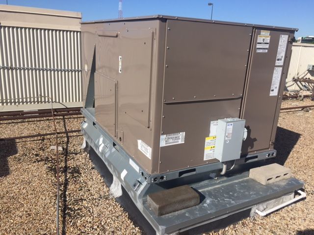 A large brown box is sitting on top of a gravel covered ground.