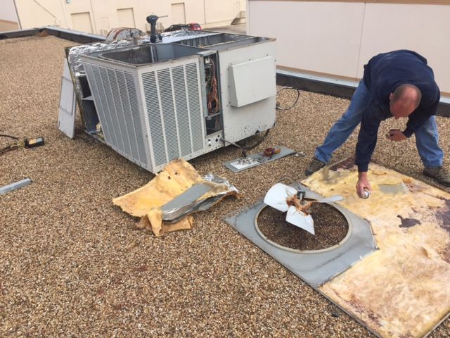 A man is working on an air conditioner on the roof of a building.