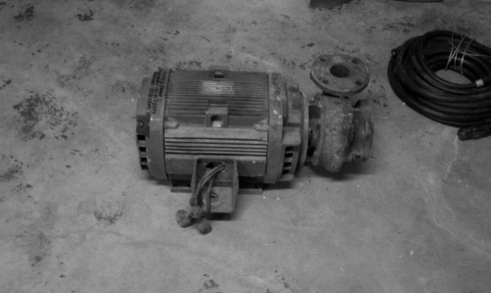 A black and white photo of an old motor on a concrete floor.
