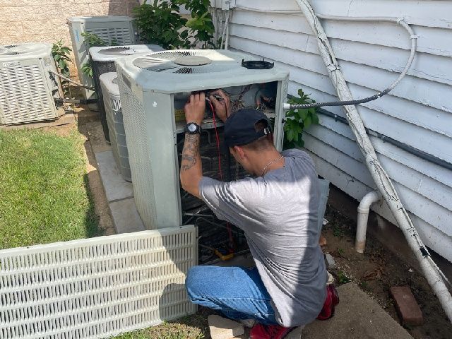 A man is working on an air conditioner outside of a house.