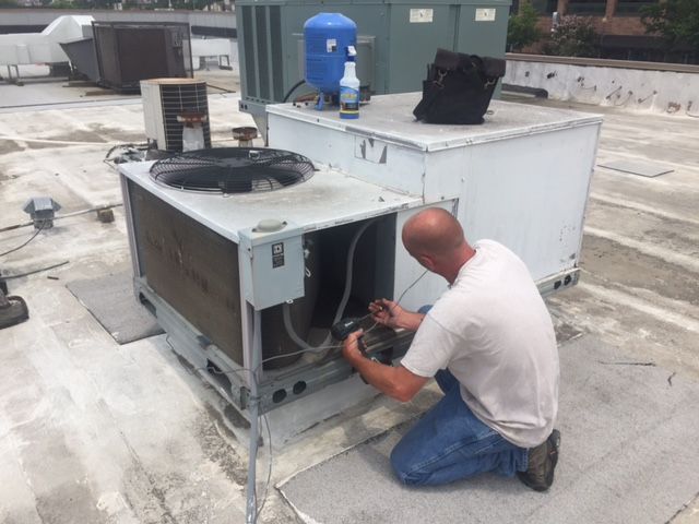 A man is working on an air conditioner on a roof.