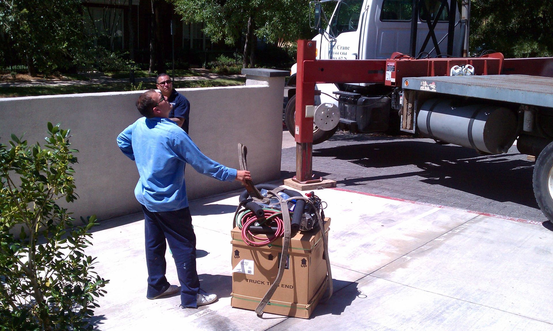 A man in a blue shirt is standing in front of a truck with a crane attached to it