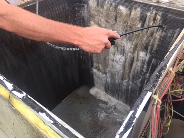 A man is cleaning a dirty air conditioner with a hose.