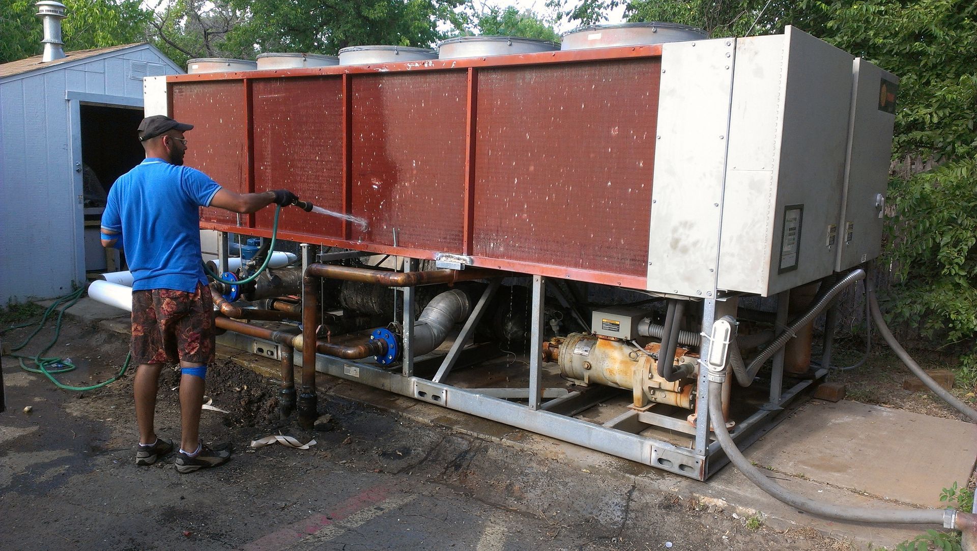A man in a blue shirt is cleaning a large machine with a hose.