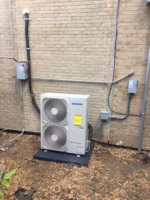 A samsung air conditioner is sitting outside of a brick building.