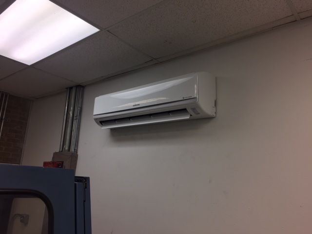 A white air conditioner is mounted on a white wall in a room.