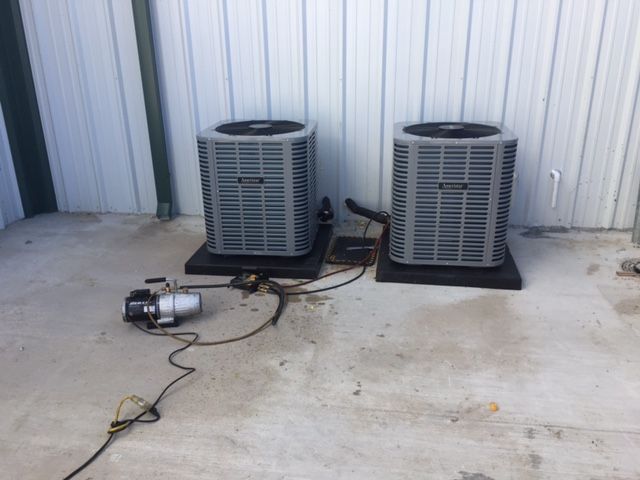 Two air conditioners are sitting next to each other on a concrete floor.