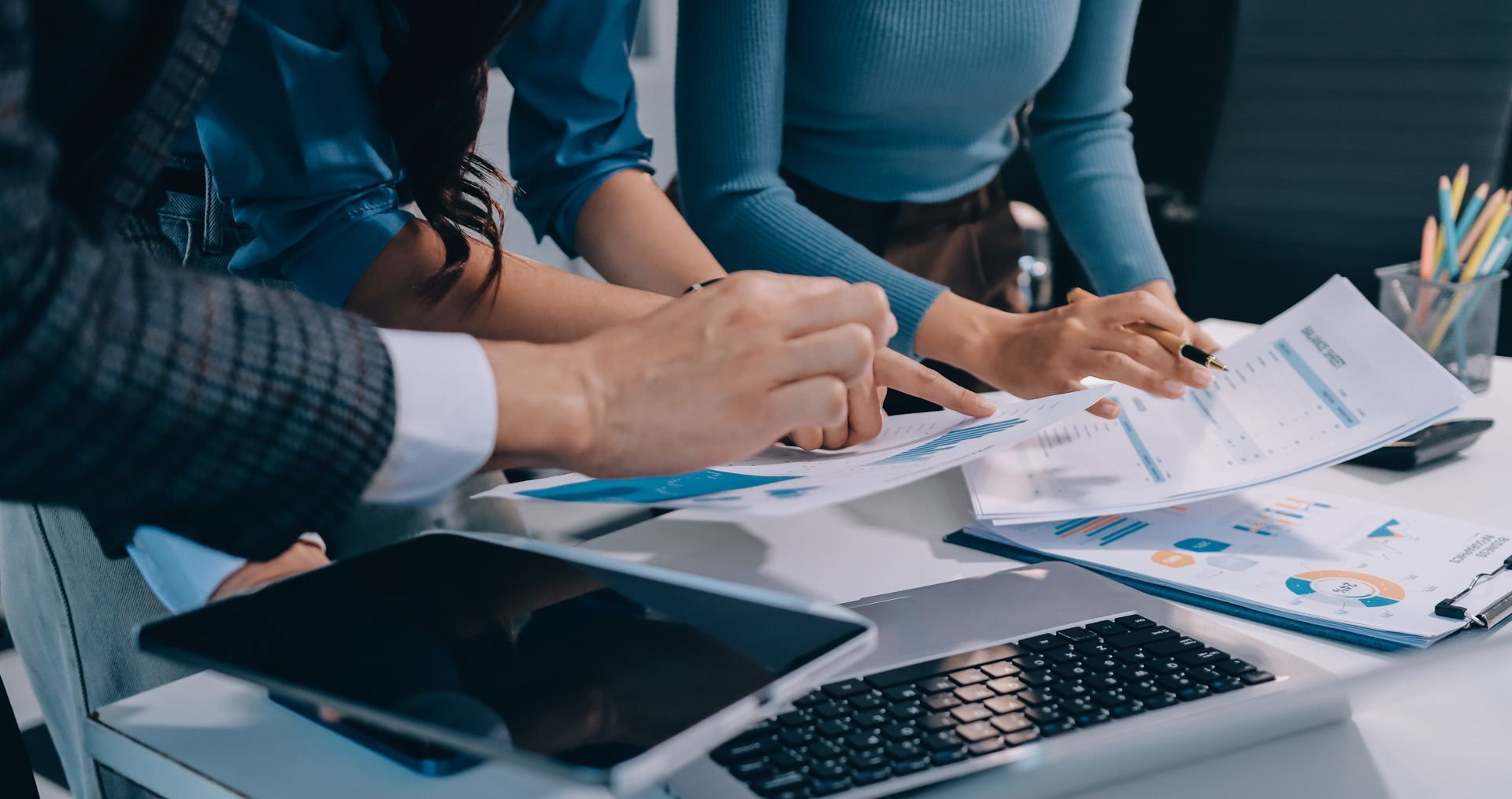People reviewing financial documents at a desk with a laptop and tablet.